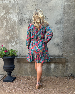 Person wearing a colorful floral dress standing on a concrete surface with a plant nearby.