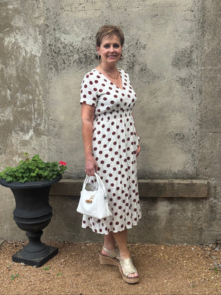 Woman in a polka dot dress standing outdoors on a concrete surface.