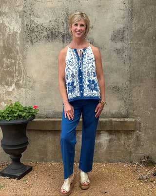 Woman wearing a blue and white patterned top and blue pants standing against a textured wall.
