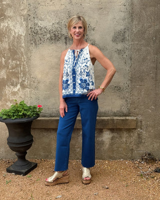 Woman wearing a blue and white patterned top and blue pants standing against a textured wall.