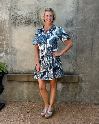 Woman wearing a blue and white floral dress standing against a textured wall.