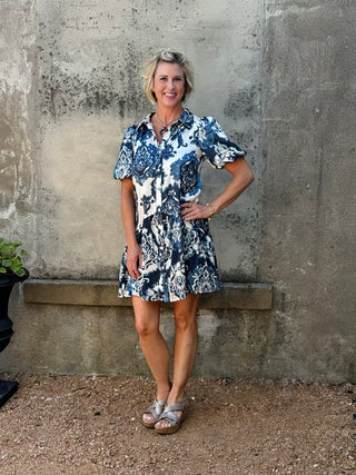Woman wearing a blue and white floral dress standing against a textured wall.