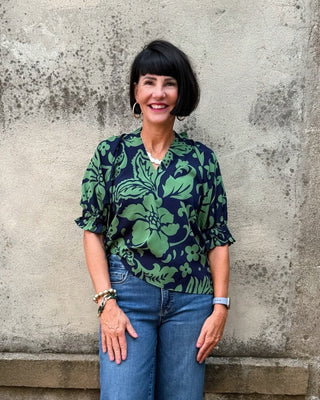 Woman wearing a floral blouse and blue jeans standing against a textured wall.