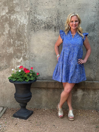 Woman in a blue dress standing on a concrete surface with a potted plant nearby.