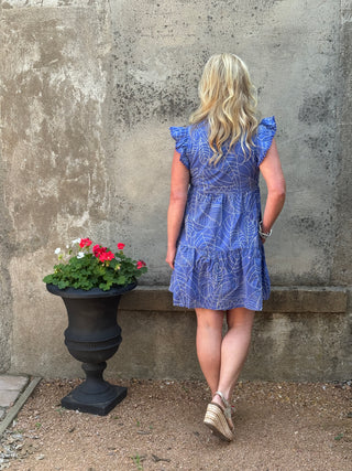 Person wearing a blue dress standing next to a potted plant on a concrete surface