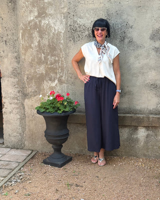 Person standing next to a potted plant with red flowers on a concrete surface