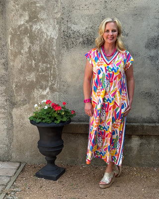 Woman in a colorful dress standing on a concrete surface with a potted plant nearby.