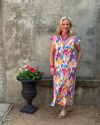 Woman in a colorful dress standing on a concrete surface with a potted plant nearby.