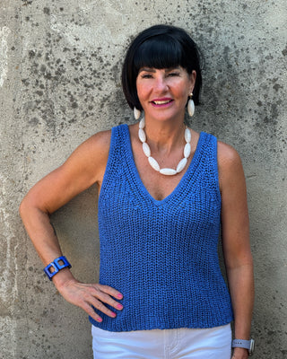 Woman wearing a blue sleeveless top and white pants against a textured wall.