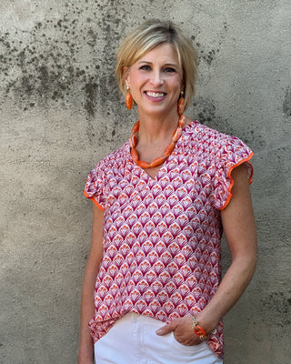 Woman wearing a patterned top with orange trim against a textured wall