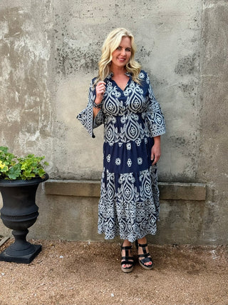 Woman wearing a blue and white patterned dress standing against a textured wall.