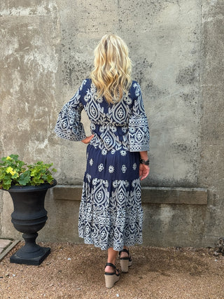 Woman wearing a blue and white patterned dress standing against a textured wall.