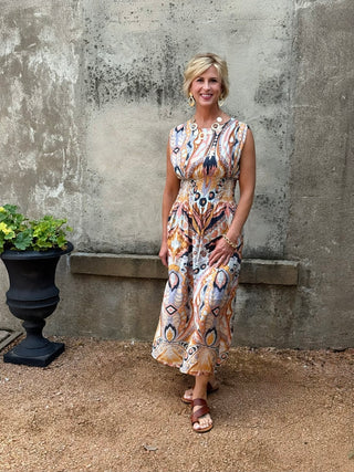 Woman in a patterned dress standing against a textured wall with a pot of flowers.