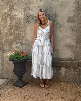 Woman in a white dress standing on a stone path with a plant pot containing red flowers.