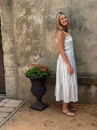 Woman in a striped dress standing next to a potted plant on a concrete floor.