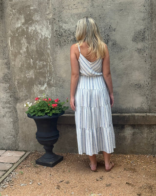 Woman in a striped dress standing next to a potted plant against a textured wall.
