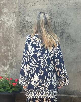 Person wearing a navy and white floral outfit standing next to a stone wall and flower pot.