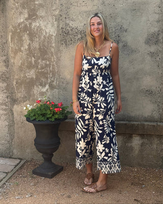 Woman in a floral dress standing next to a stone wall with a potted plant.