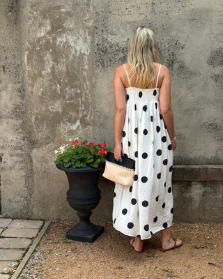 Woman in a polka dot dress standing next to a potted plant against a textured wall.