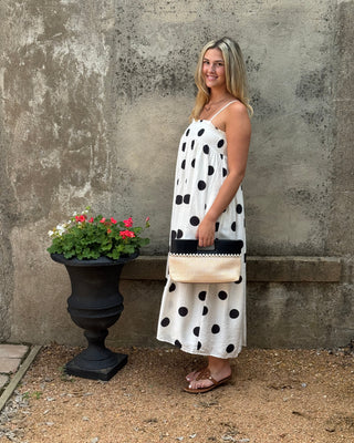Woman in a polka dot dress standing next to a potted plant against a textured wall.