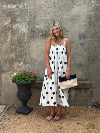 Woman in a polka dot dress standing next to a potted plant against a textured wall.