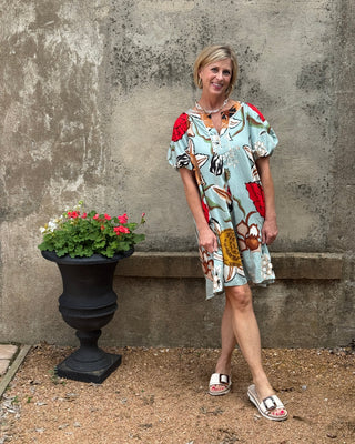 Woman in a patterned dress standing next to a potted plant against a textured wall.