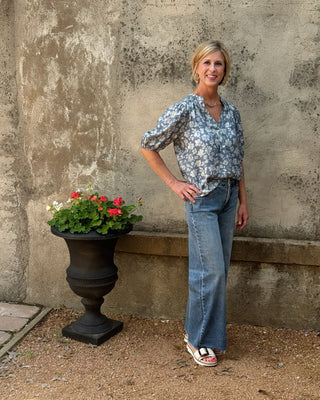 Woman standing next to a stone wall with a planter of flowers