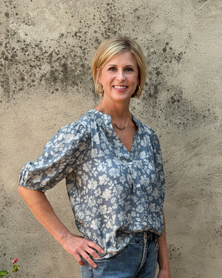 Woman wearing a blue floral blouse and jeans standing against a textured wall.