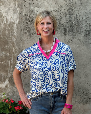 Woman wearing a blue and white patterned shirt with pink accents against a textured wall.