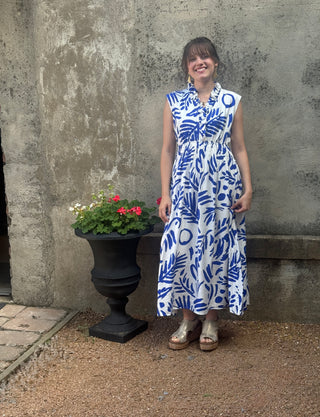 Woman in a blue and white dress standing next to a stone wall with a flower pot.