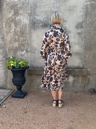 Person wearing a leopard print dress standing on a concrete surface with a plant nearby.