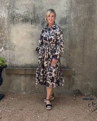Woman in a floral dress standing against a textured wall.