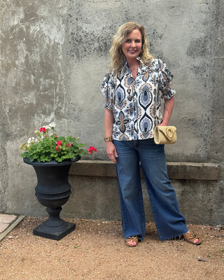 Woman standing outdoors next to a potted plant against a concrete wall.