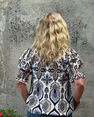 Person wearing a patterned blouse standing against a textured wall.