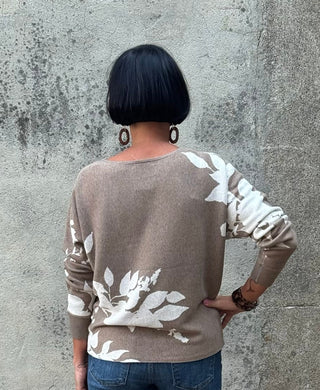 Person wearing a patterned sweater and jeans standing against a textured wall.