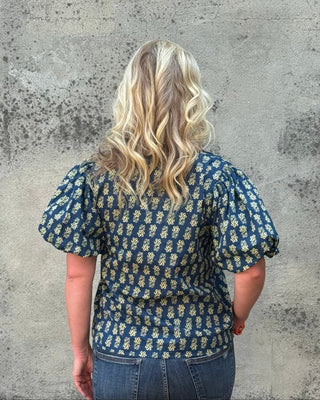 Person wearing a blue floral blouse against a textured gray wall