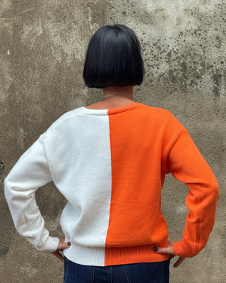 Person wearing a two-tone orange and white sweater on a concrete floor.