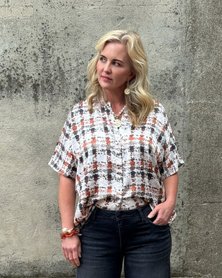 Woman wearing a plaid shirt and dark jeans standing against a textured wall.
