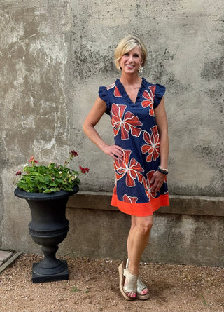 Woman in  navy dress with orange abstract flower print against a concrete wall