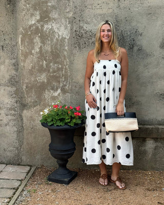Woman in a polka dot dress standing next to a potted plant against a textured wall.