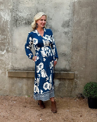 Woman wearing a blue floral dress standing against a textured wall.