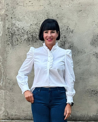 Woman wearing a white blouse and blue pants standing against a textured wall.