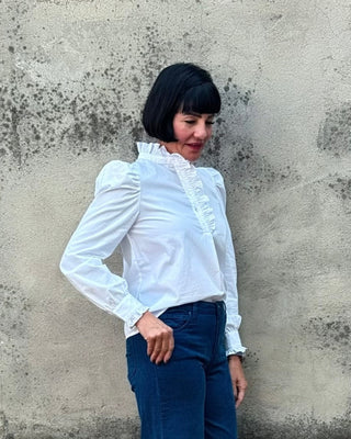 Woman in a white shirt and blue pants standing against a textured wall.