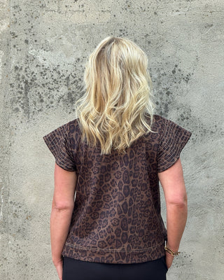 Person wearing a leopard print top against a textured wall
