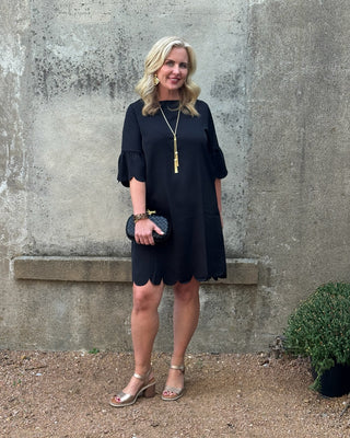 Woman in a black dress standing against a textured wall.