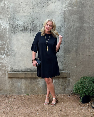 Woman in a black dress standing against a textured wall.