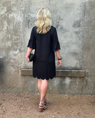 Woman wearing a black dress standing against a textured wall.