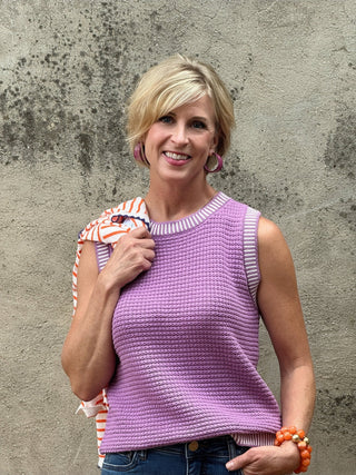 woman in sleeveless lavendar waffle textured top against a concrete wall