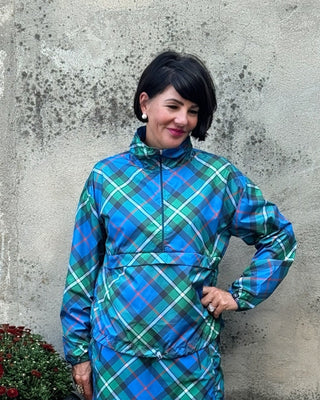 Person wearing a blue plaid dress standing against a textured wall with a potted plant nearby.