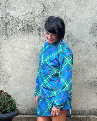 Person wearing a blue plaid outfit standing next to a textured wall and potted plant.